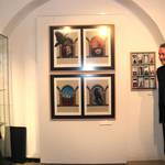 Der Künstler Jörg Wachtel (rechts) übergibt seine Digigraphien zur Ausstellung an Museumsleiterin Dr. Heise (links). Die Digigraphien hängen an einer Wand zwischen den beiden.